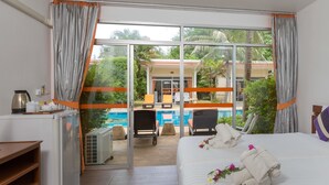 A hotel room with a large sliding glass door leading to a pool area, a bed with towels, and a small kitchenette. - Phuket Sea Resort (Rawai)
