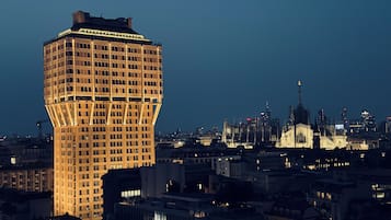 Un immeuble de grande hauteur doté d’une façade originale, à motifs géométriques, et de nombreuses fenêtres, entouré d’autres bâtiments et d’une structure imposante qui ressemble à une cathédrale, mais qui se trouve au loin.