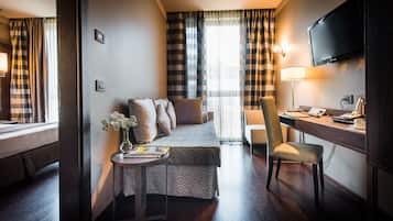 A hotel room with a bed, a desk with a chair, a TV, and a window with curtains.