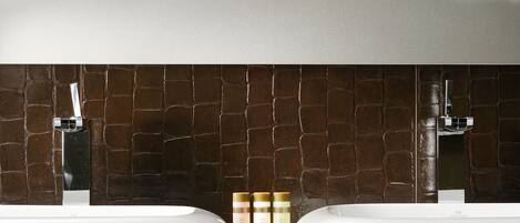 A bathroom with a marble countertop, two sinks, and a tiled wall with a tufted design.