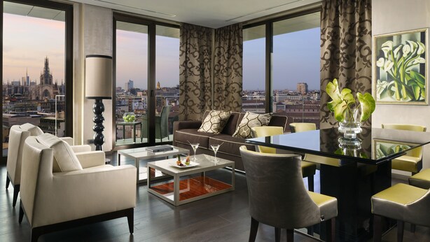 A modern living room with a city view, a glass coffee table, and a dining area with yellow chairs.