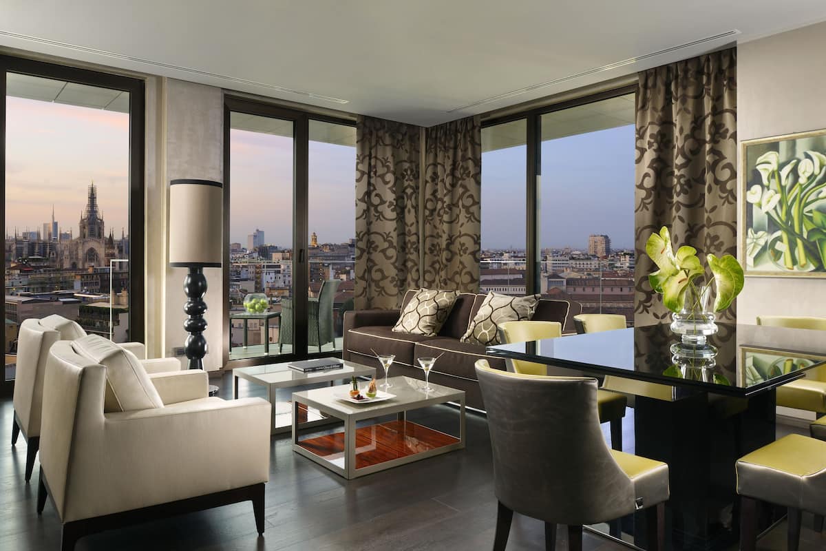 A modern living room with a city view, a glass coffee table, and a dining area with yellow chairs.