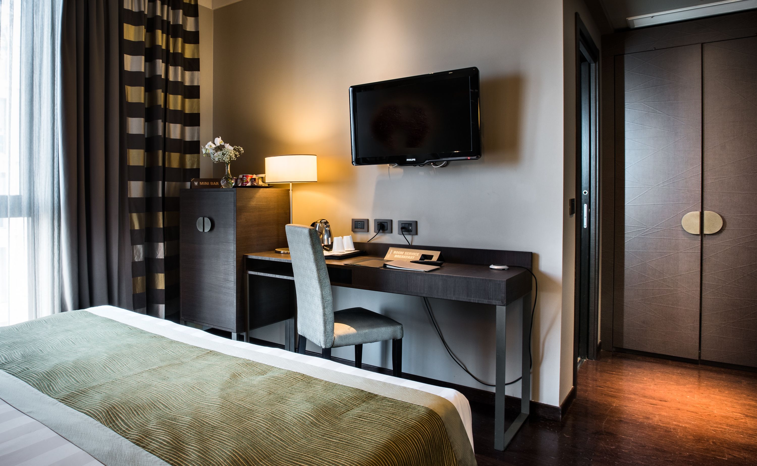 Una habitación de hotel con una cama, un escritorio con una silla, un televisor y un minibar.