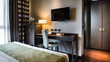 Una habitación de hotel con una cama, un escritorio con una silla, un televisor y un minibar.