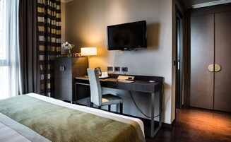 Una habitación de hotel con una cama, un escritorio con una silla, un televisor y un minibar.