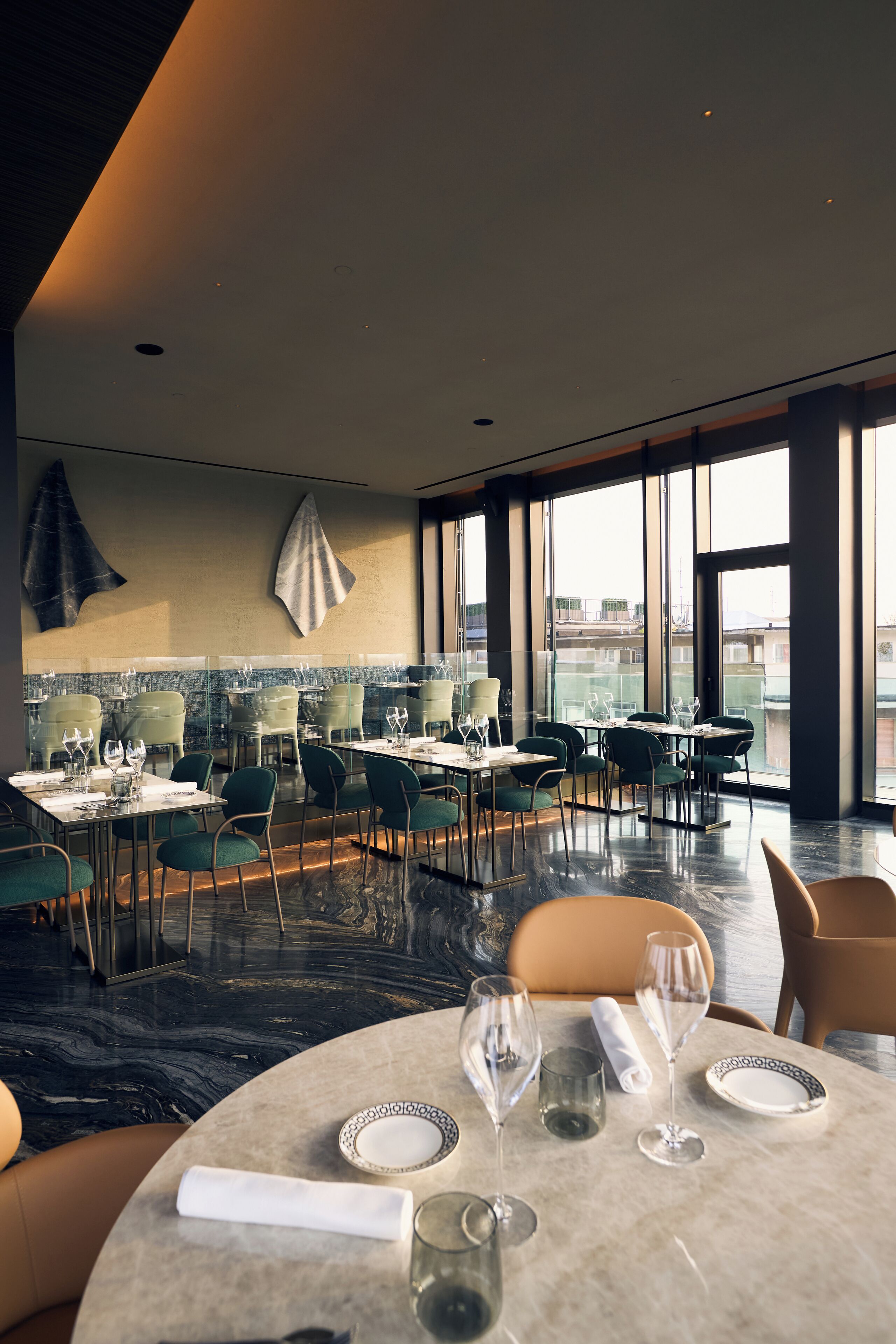 A modern restaurant with high ceilings, large windows, and a mix of table and booth seating.