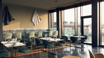 A modern restaurant with high ceilings, large windows, and a mix of table and booth seating.