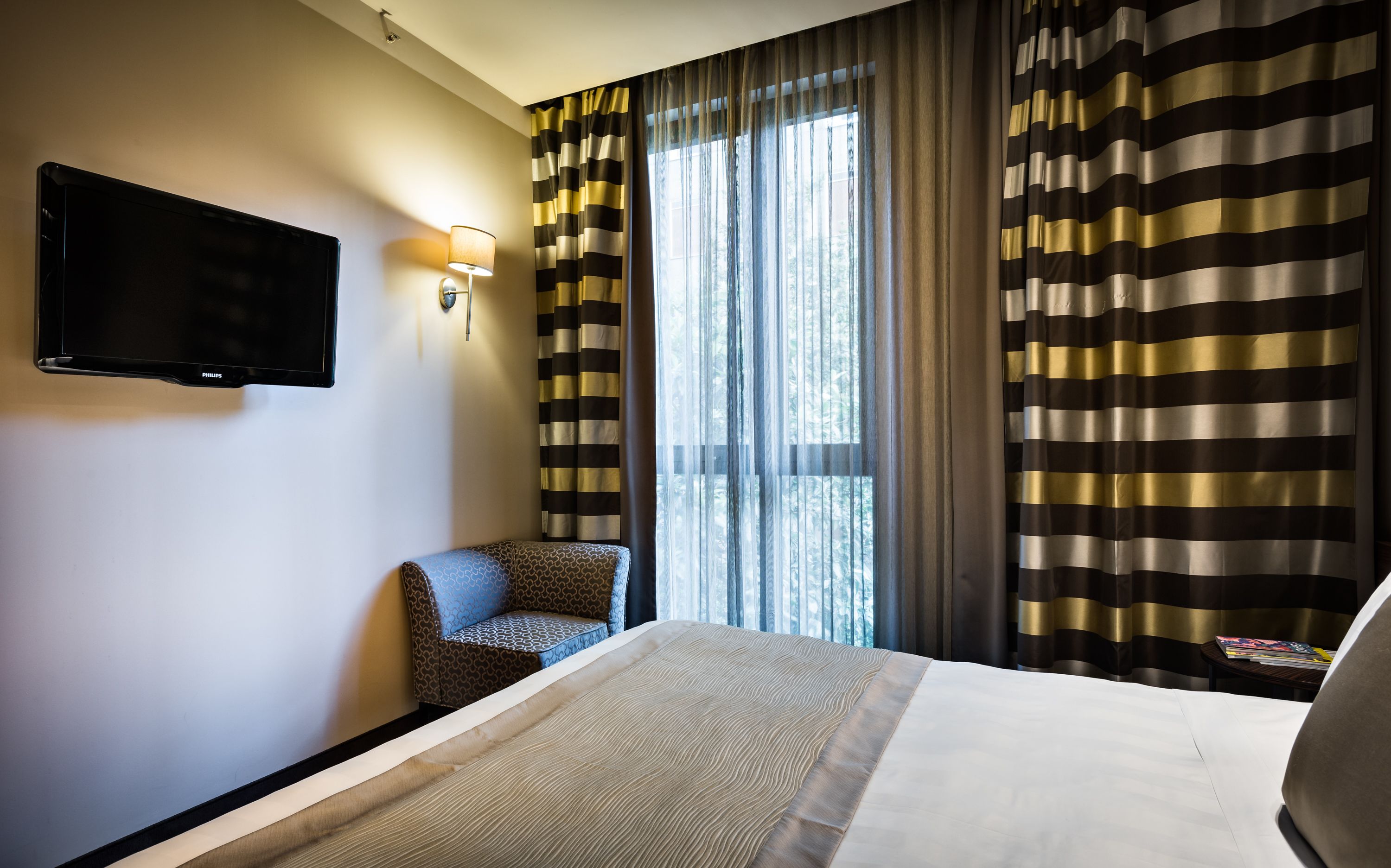 A hotel room with a bed, a television mounted on the wall, a chair, and curtains.
