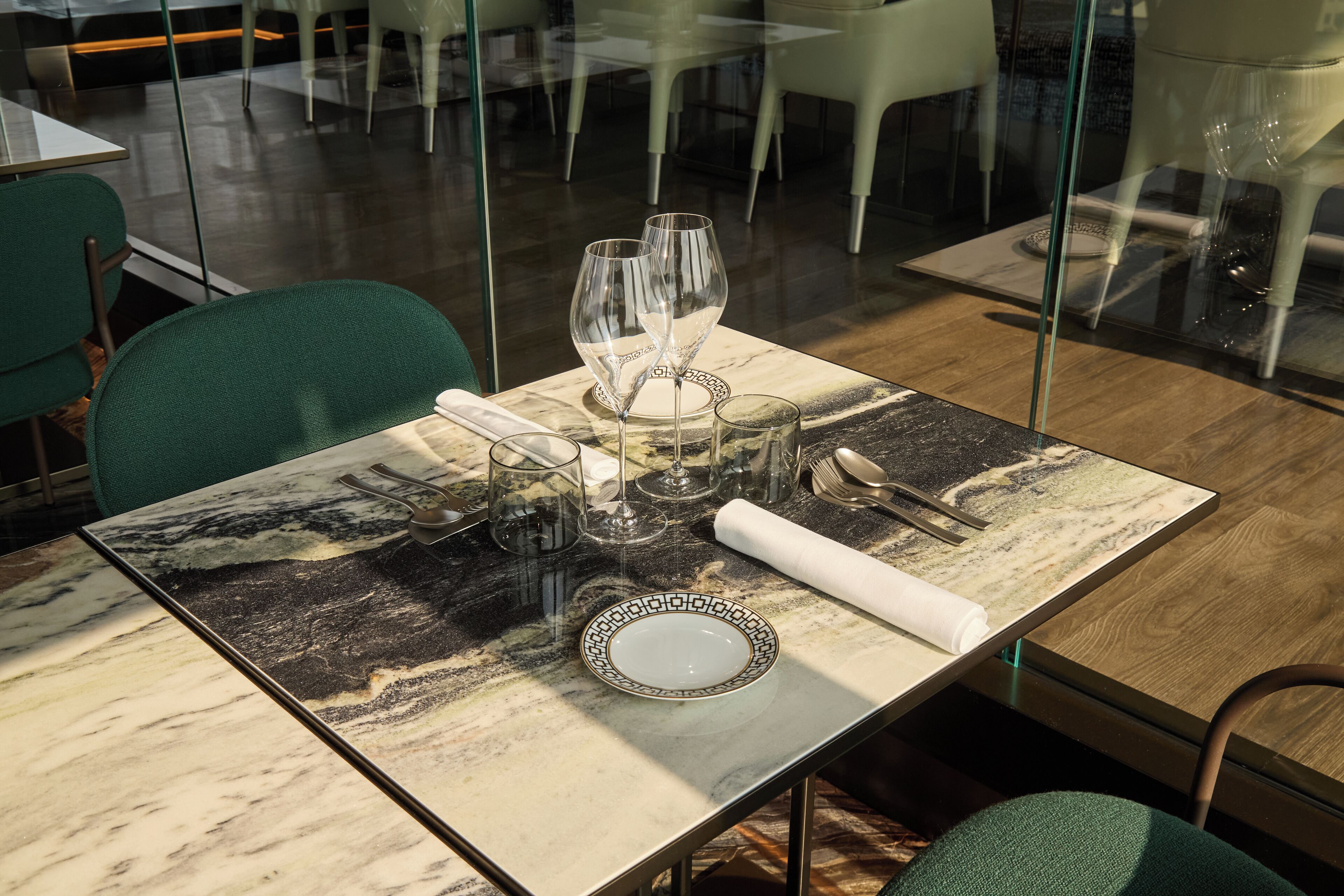 Una mesa de comedor con cubierta de mármol, copas de cristal transparente y un plato decorativo.