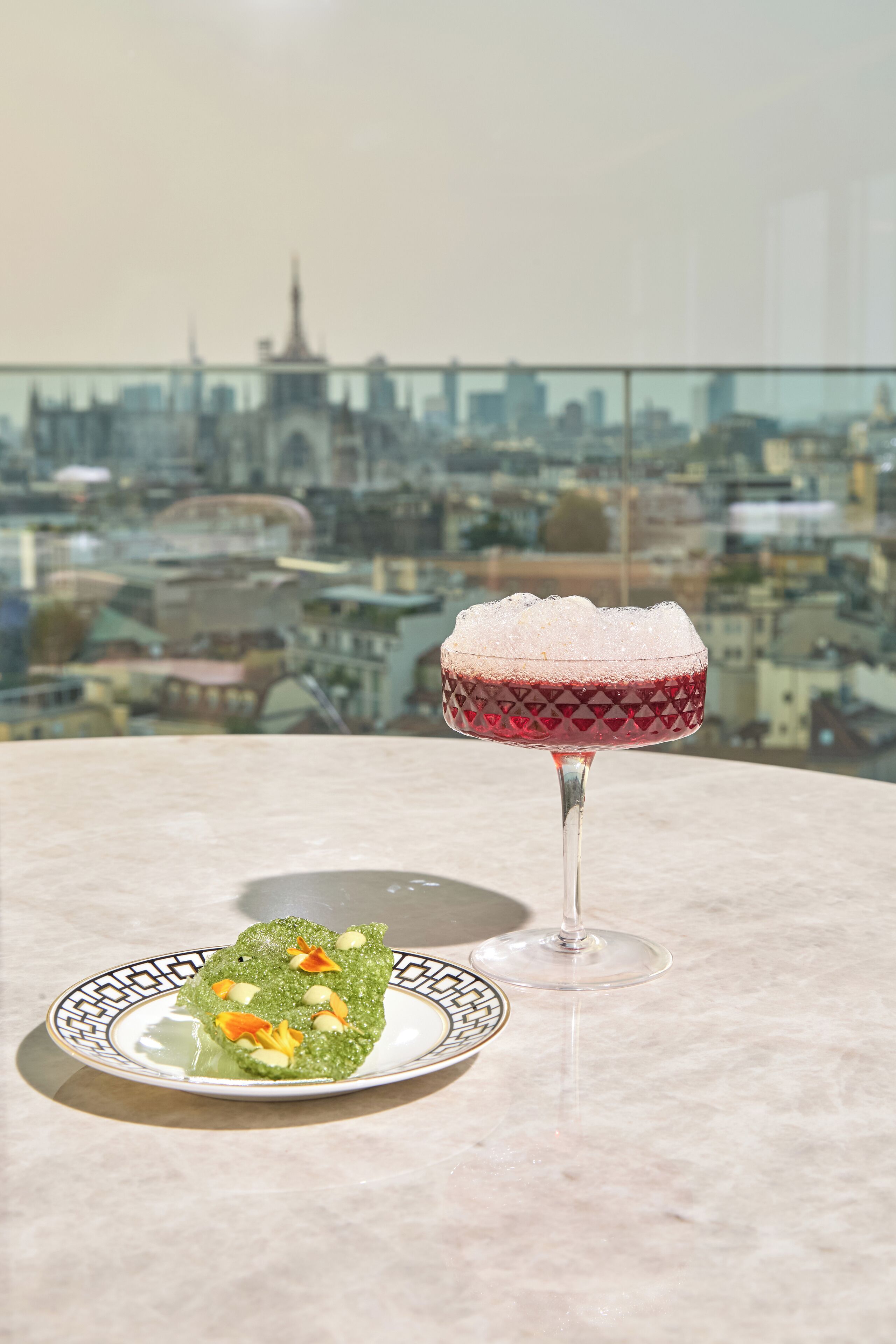 Un bicchiere da martini con cubetti di ghiaccio su un tavolo, con vista sulla città sullo sfondo.
