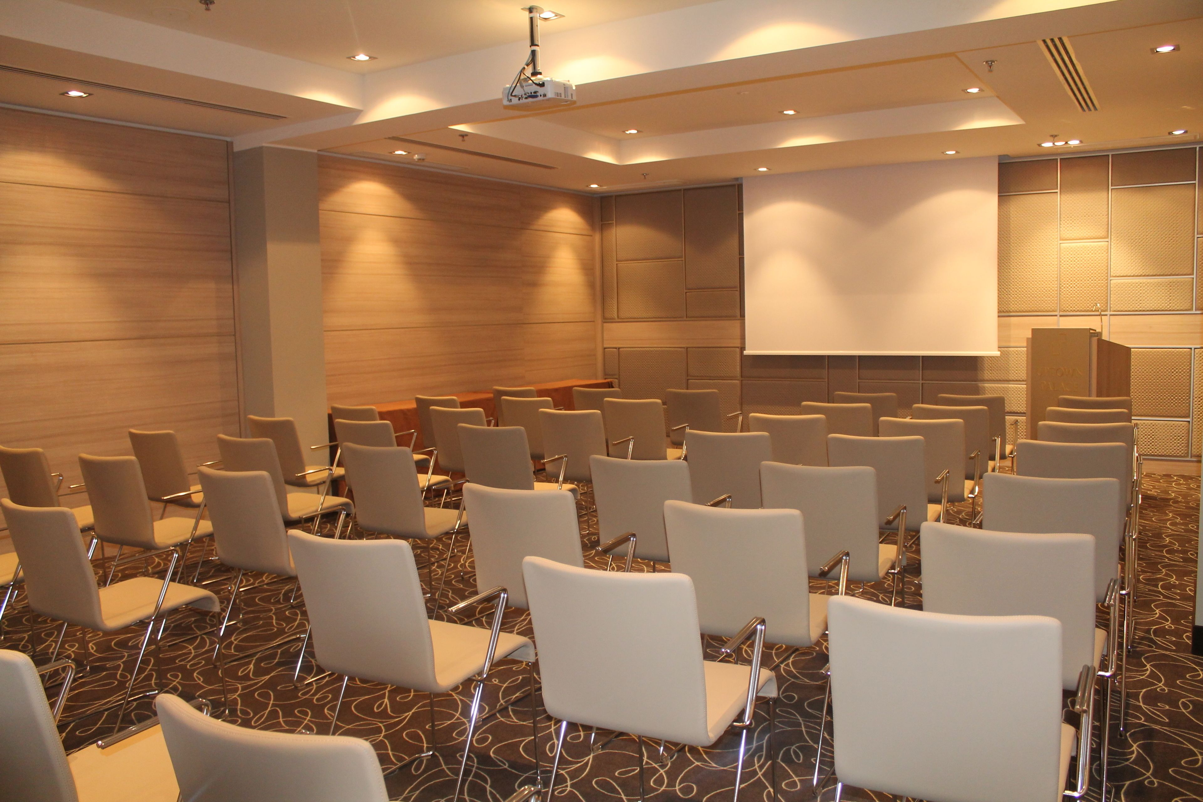 A conference room with rows of white chairs, a large screen, and a podium.