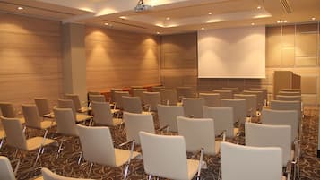 A conference room with rows of white chairs, a large screen, and a podium.