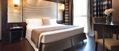Ein modernes Hotelzimmer mit einem großen Bett, einem Nachttisch, einem Sessel und einem Schreibtisch mit Blumen.