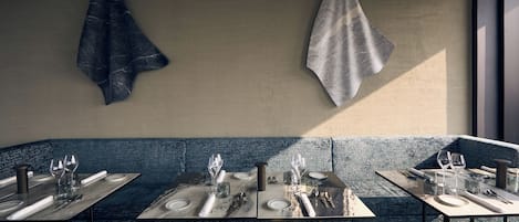 Un restaurante con una decoración moderna, que presenta un banco azul con textura, mesas con cubierta de mármol y una estética minimalista.