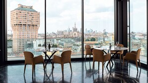 A modern hotel room with a large panoramic window, a marble floor, and a dining area with chairs and a table.