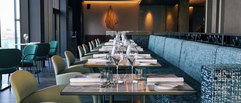 A modern restaurant with a long dining table set for a meal, surrounded by cushioned seating.