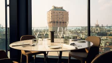 Uma mesa de jantar com cadeiras e copos de vinho montada numa varanda com vista para a cidade.