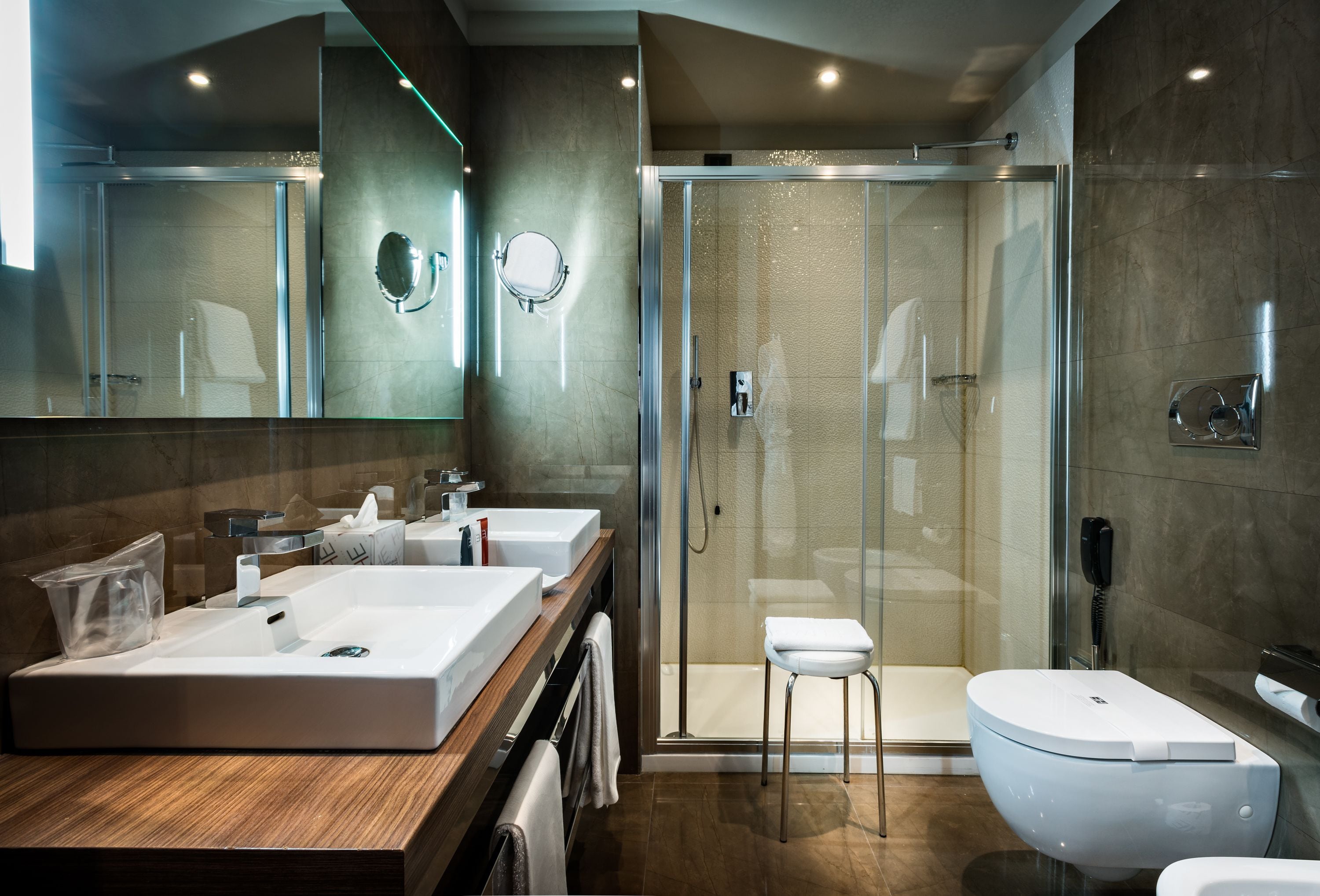 Ein modernes Badezimmer mit zwei Waschbecken, einer Duschkabine aus Glas und einer Toilette.