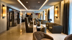 A modern hotel lobby with a marble floor, comfortable seating areas, and a television screen.