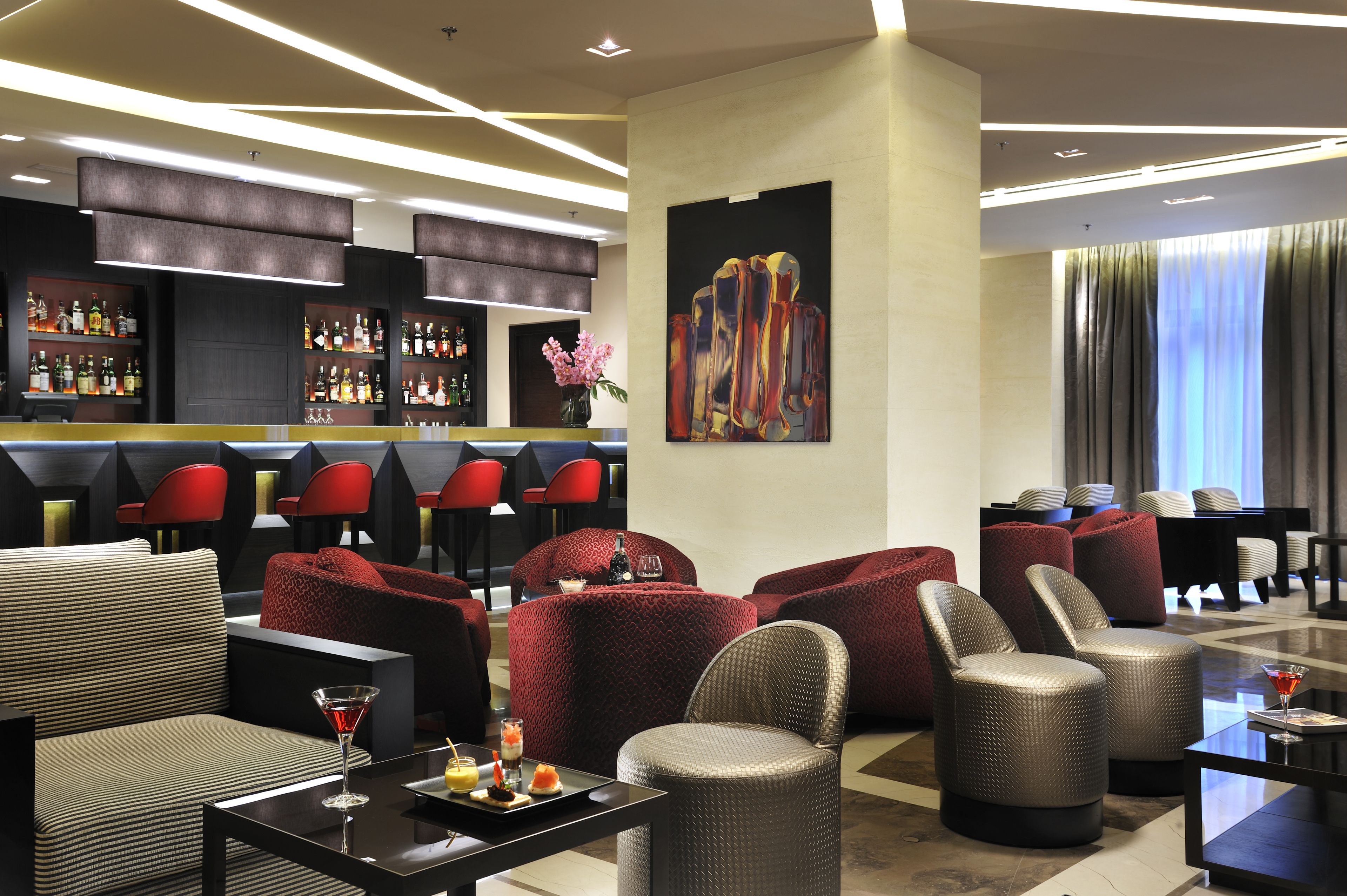 A modern lounge area with seating, a bar, and a large abstract painting.