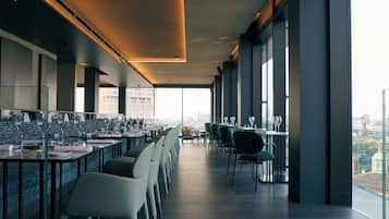 En moderne restaurant med en lang disk, flere borde og stole. Restauranten har store vinduer og udsigt over byen.