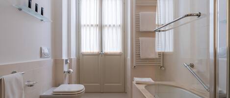 A modern bathroom with a sink, toilet, and bathtub. There is a window with curtains, a towel rack, and a shelf with toiletries.