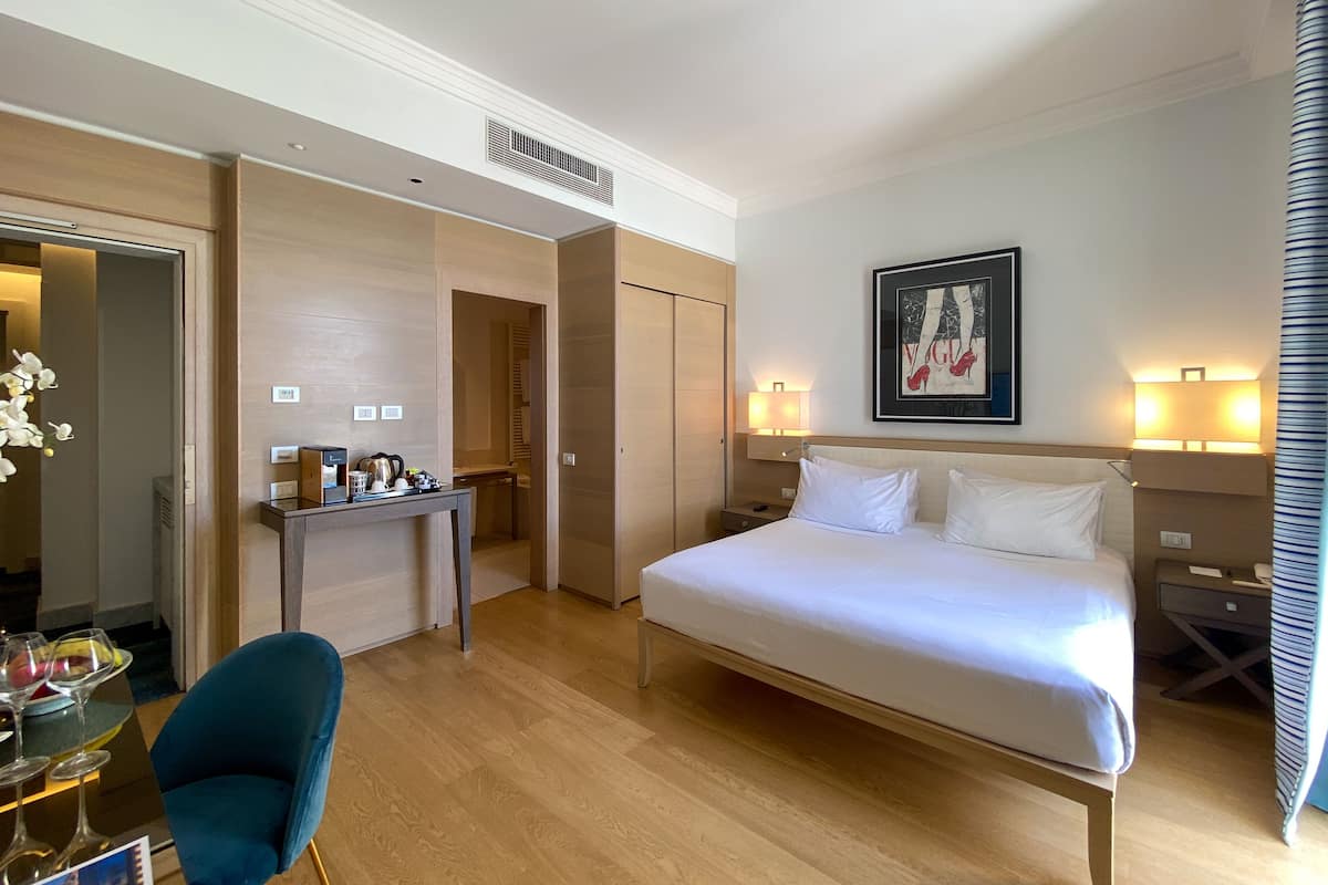 Ein Hotelzimmer mit einem Bett, Nachttischen, einem Schreibtisch mit Stuhl und einem gerahmten Bild an der Wand.