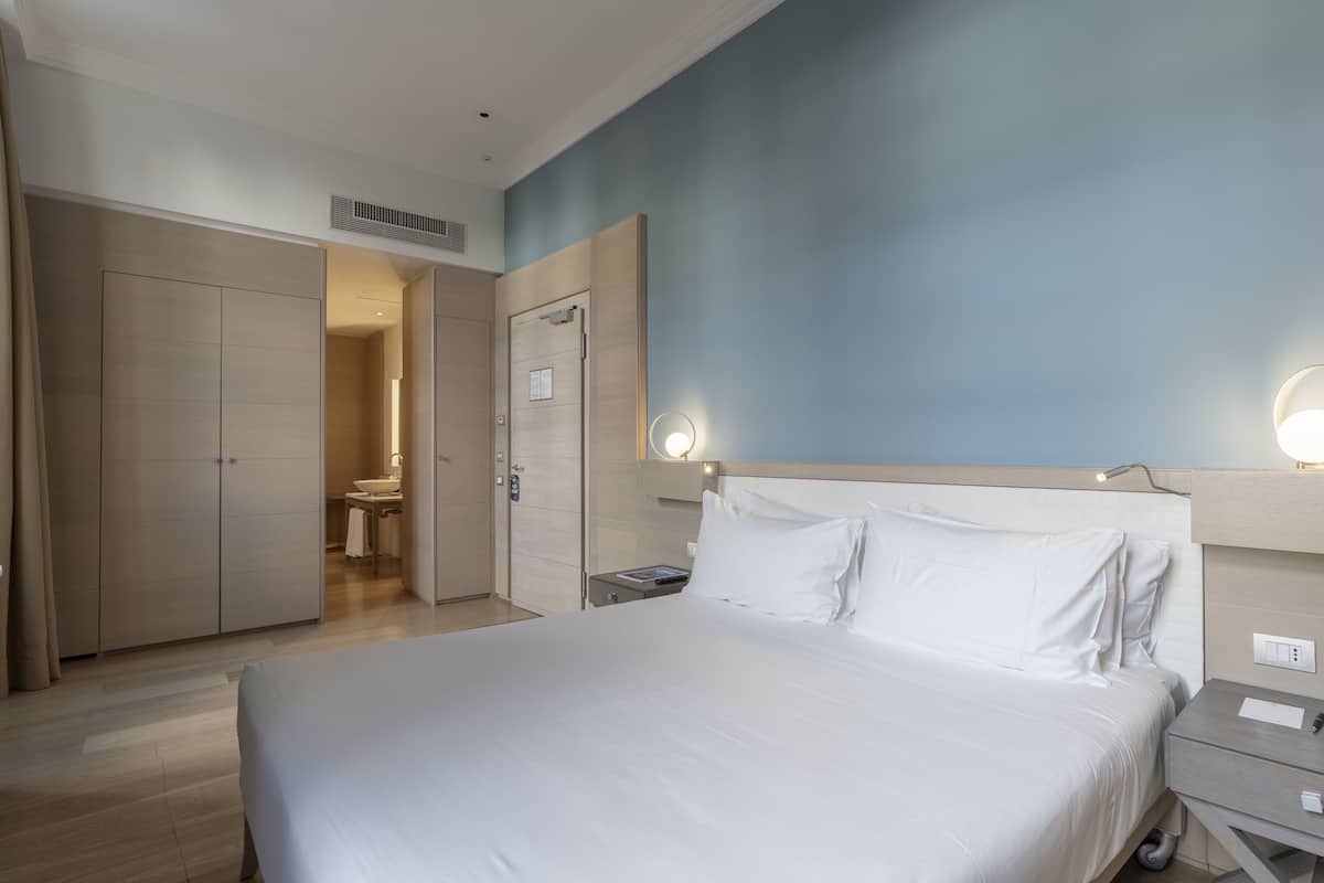Ein Hotelzimmer mit einem großen Bett, einem Nachttisch, einem Schrank und einem sichtbaren Badezimmer durch eine offene Tür.