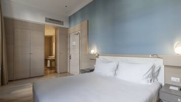 A hotel room with a large bed, a bedside table, a nightstand, a wardrobe, and a bathroom visible through an open door.