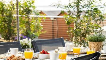 Ein Essbereich im Freien mit einem Tisch, der für das Frühstück gedeckt ist, einschließlich Croissants, Obst und Orangensaft.