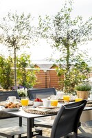 Un área de comedor al aire libre con una mesa lista para el desayuno, incluyendo cruasanes, fruta y jugo de naranja.