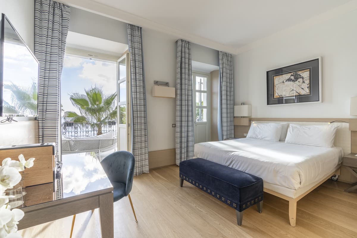 Ein Hotelzimmer mit Bett, Schreibtisch, Stuhl und Blick auf Palmen.