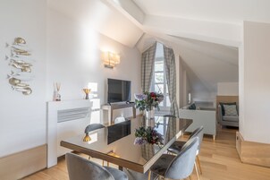 Un comedor moderno con mesa de vidrio, sillas tapizadas en gris, un televisor de pantalla plana y un elemento decorativo en la pared.