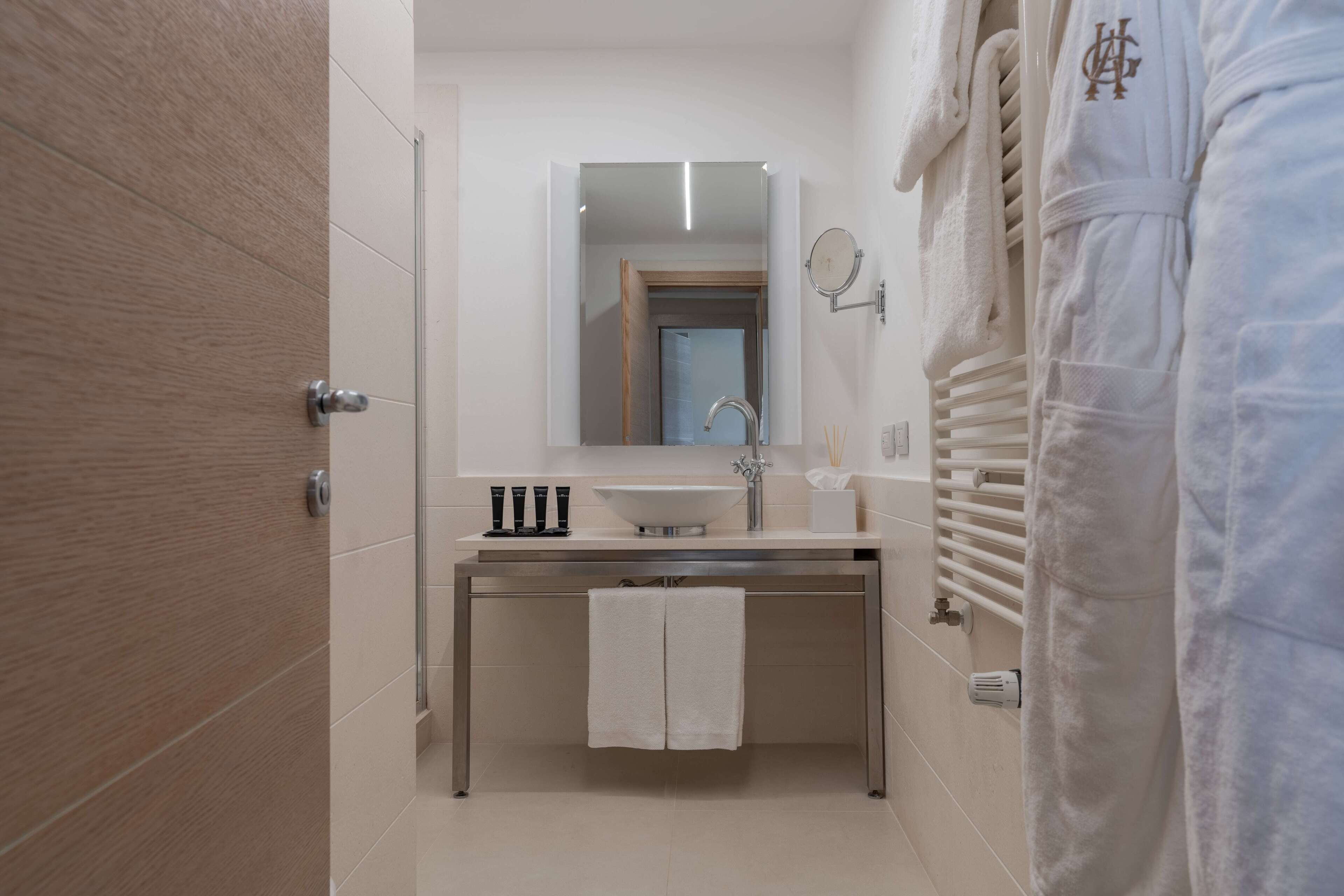Ein modernes Badezimmer mit Holztür, Waschbecken und Spiegel darüber sowie einem Handtuch an der Wand.