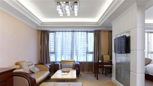 A hotel room with a sofa, a coffee table, a TV, and a large window with curtains. - Ambassador Hotel Shenzhen (Shenzhen)