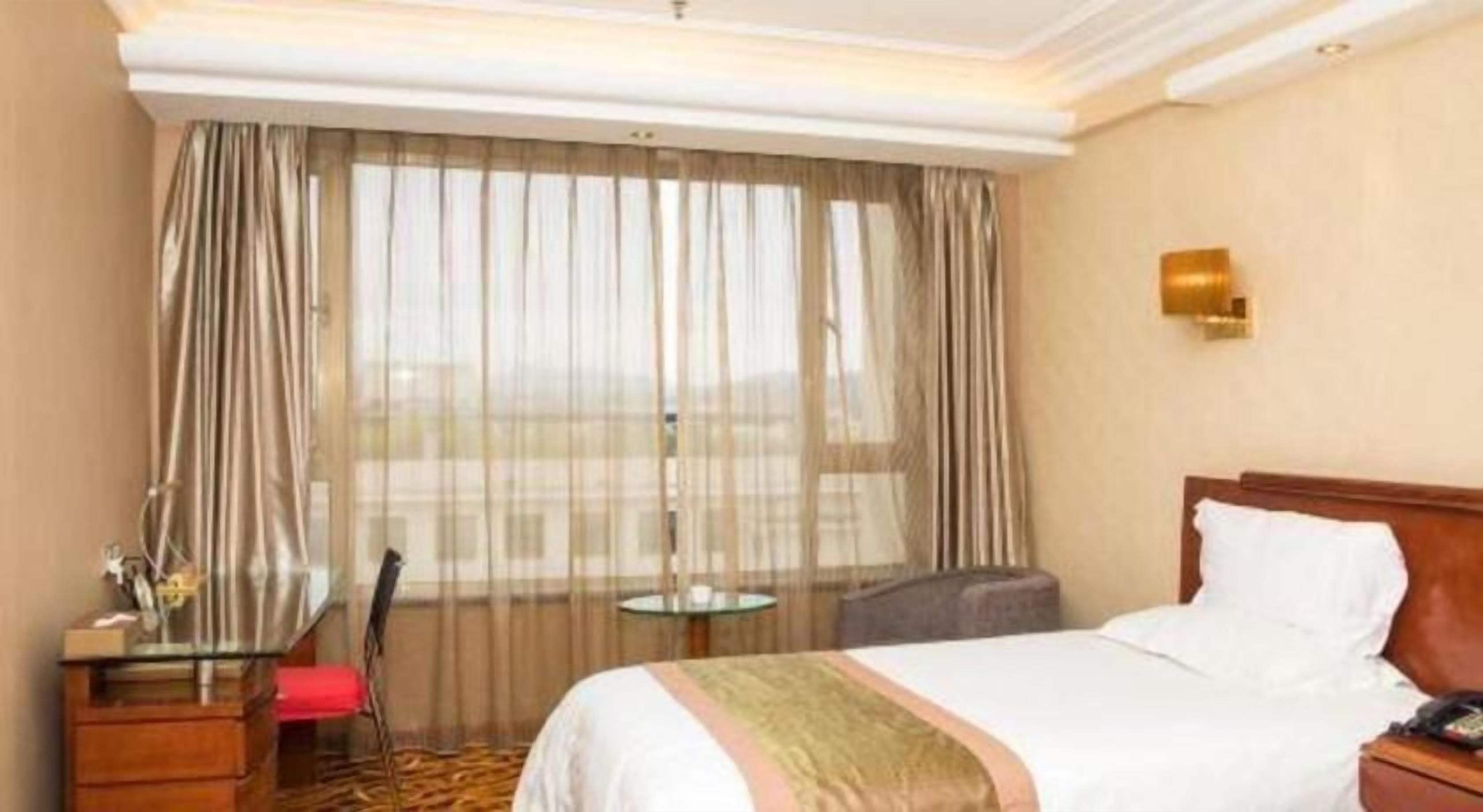 A hotel room with a bed, a desk, a chair, a small table, and a window with curtains.