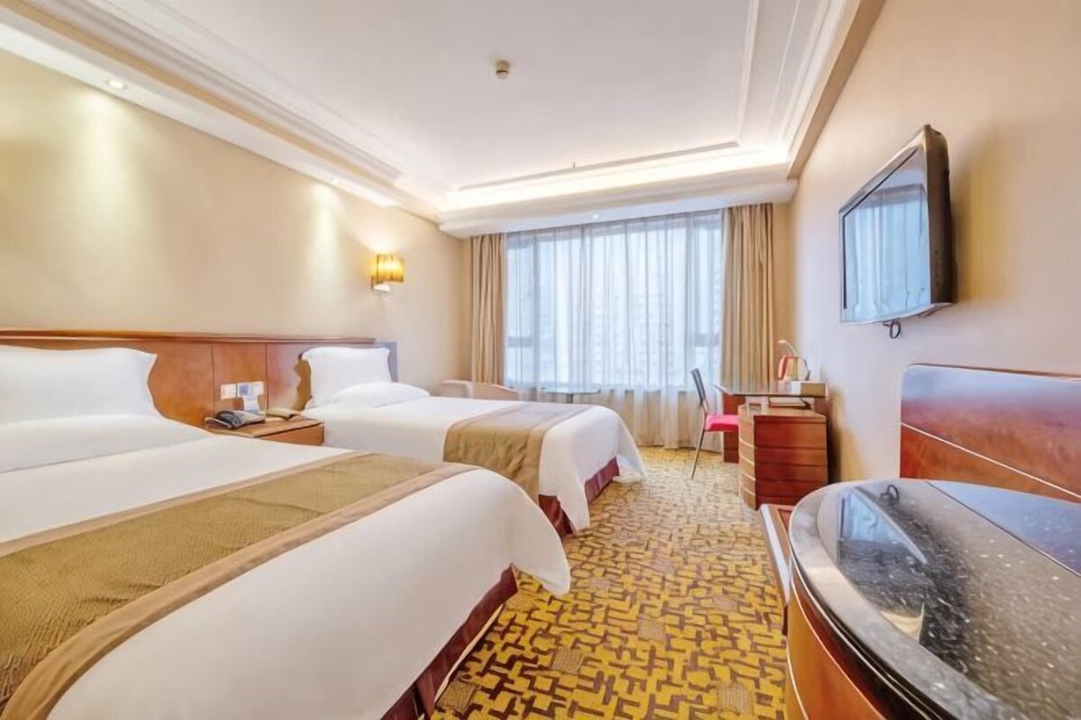 A hotel room with two beds, a desk, a chair, a television, and a large window with curtains.