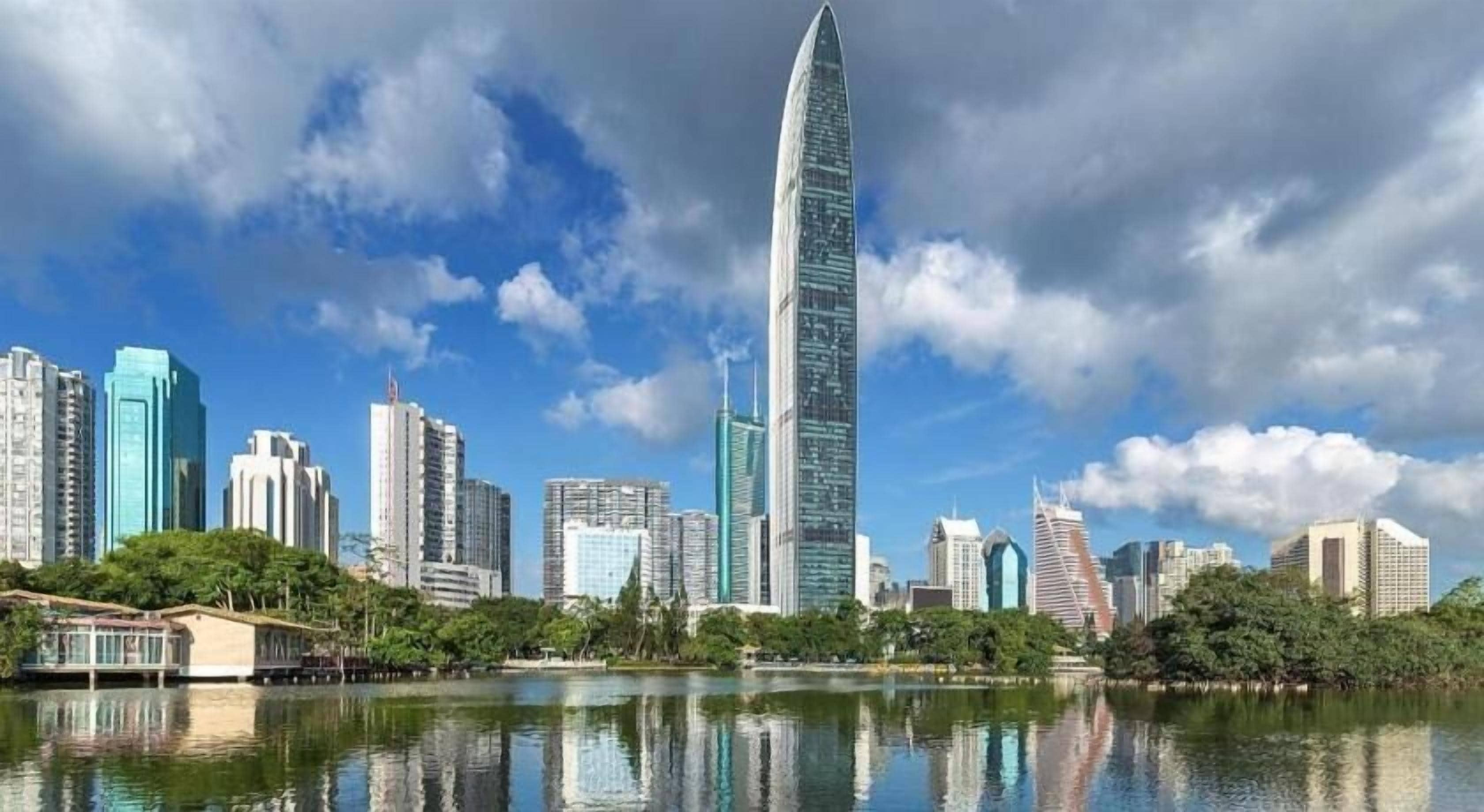 A city skyline with modern skyscrapers, a body of water reflecting the buildings, and a clear sky.
