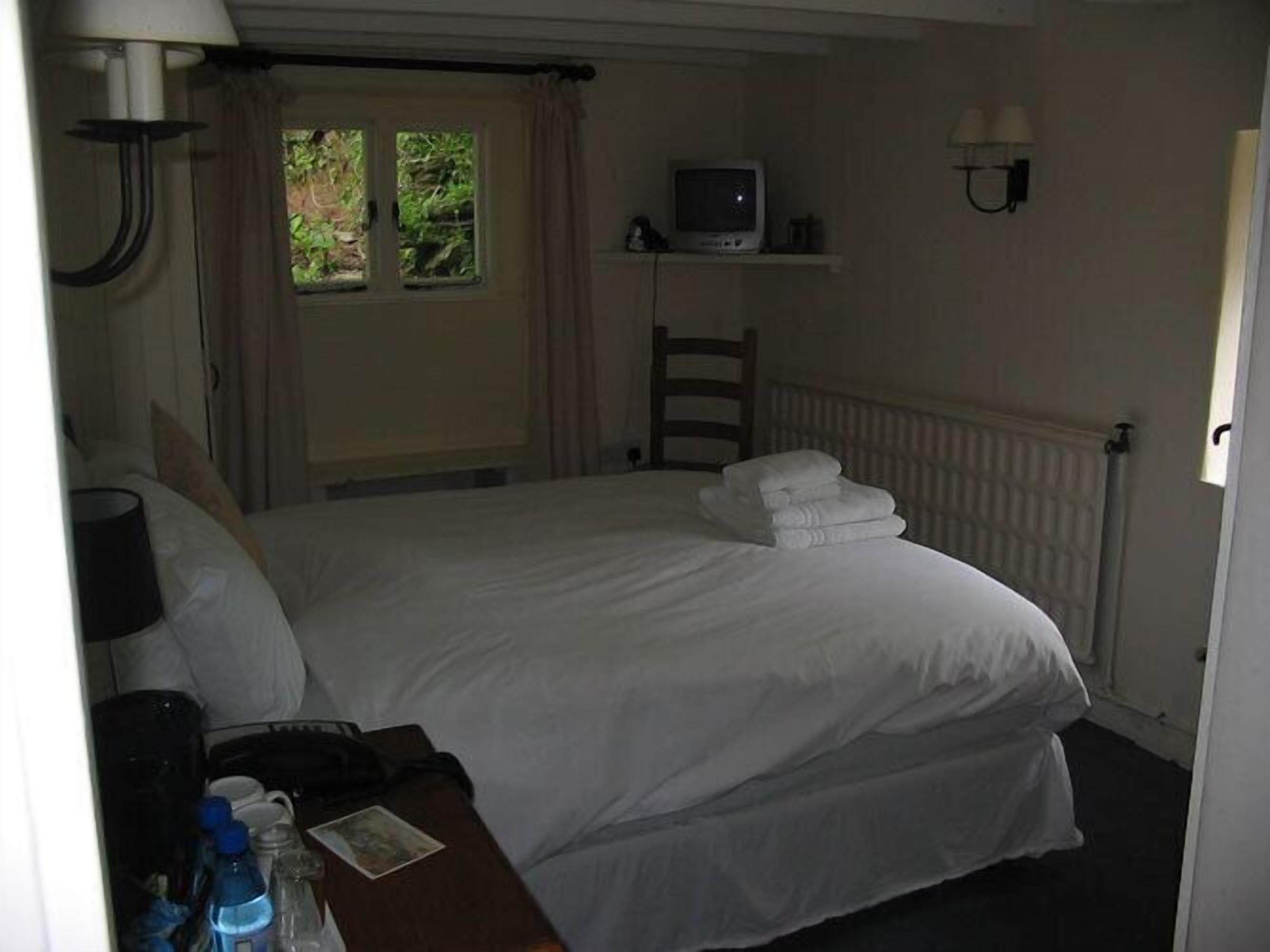 A hotel room with a bed, a TV on a shelf, a desk with a lamp, and a window with curtains.