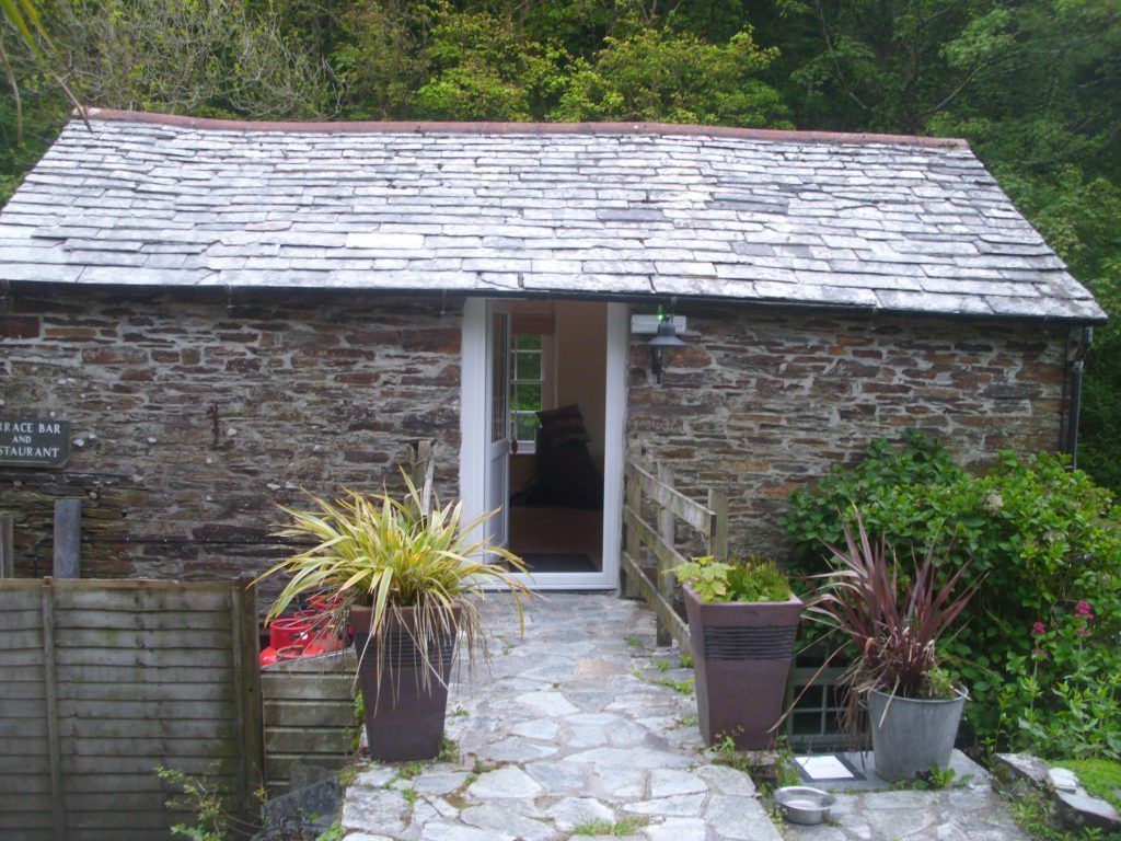 A stone building with a tiled roof, a door, and potted plants.
