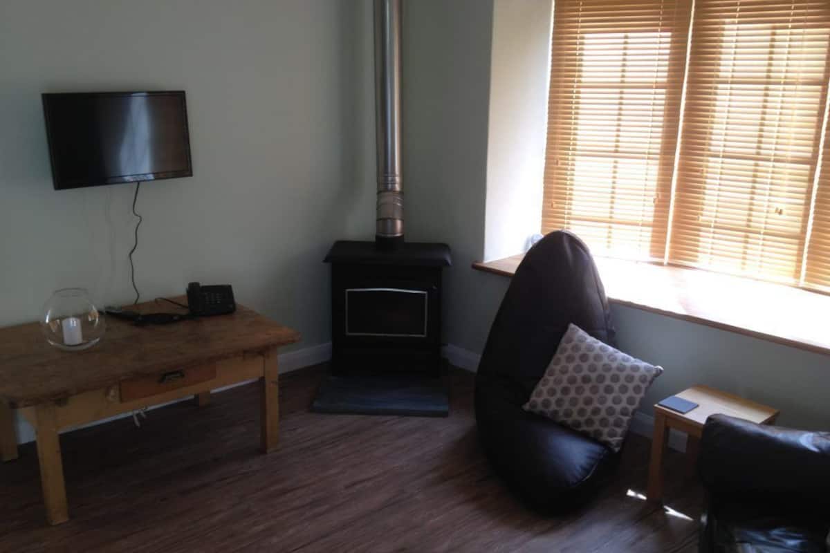 A living room with a fireplace, a television mounted on the wall, a wooden table with a glass, and a bean bag chair.