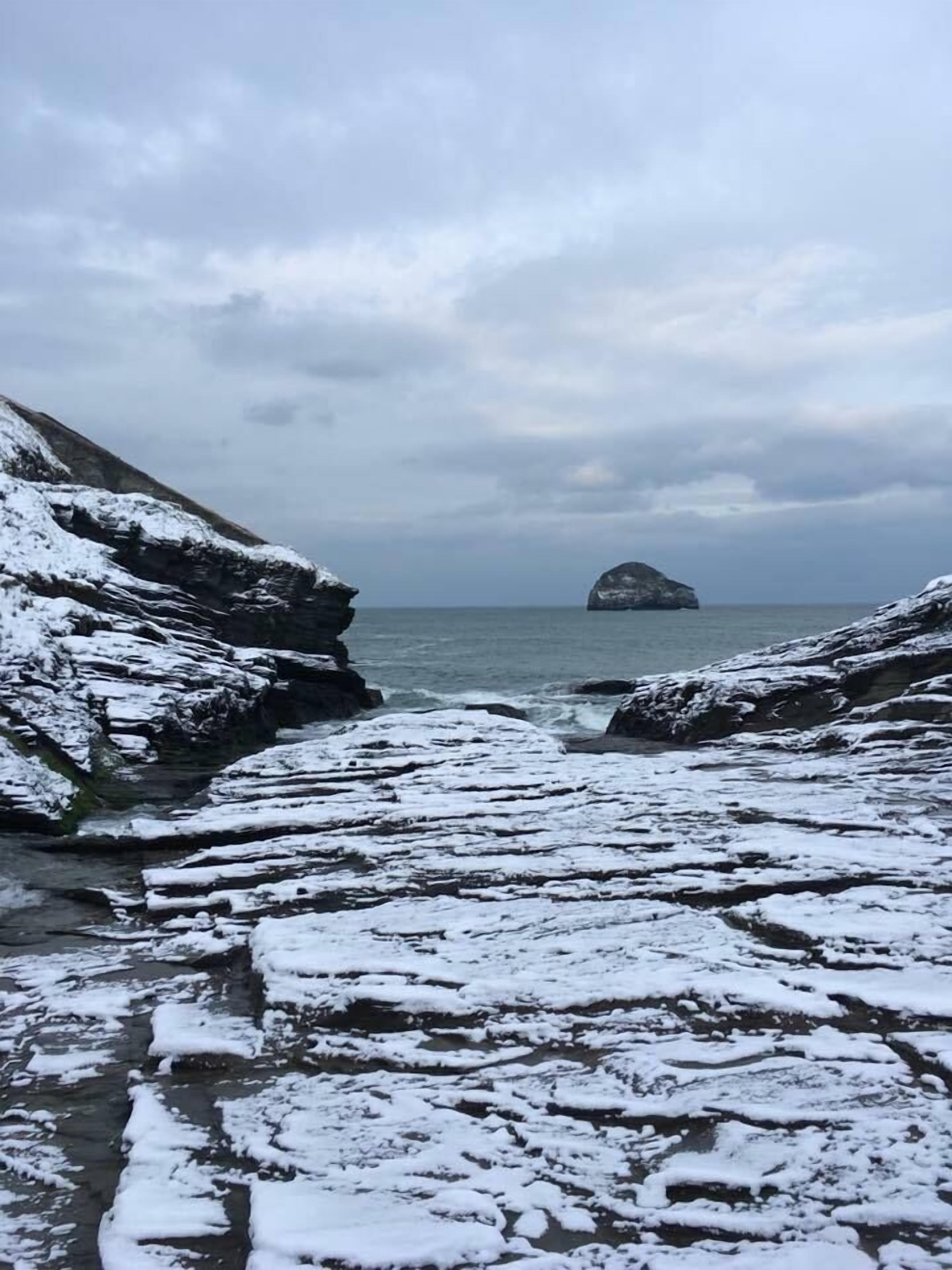 A rocky shoreline with snow-covered rocks and a distant island.