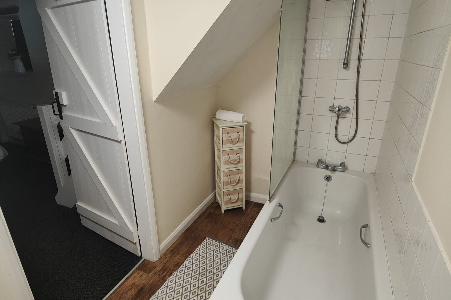 Une salle de bain avec une baignoire blanche, une petite commode en bois et un espace douche.