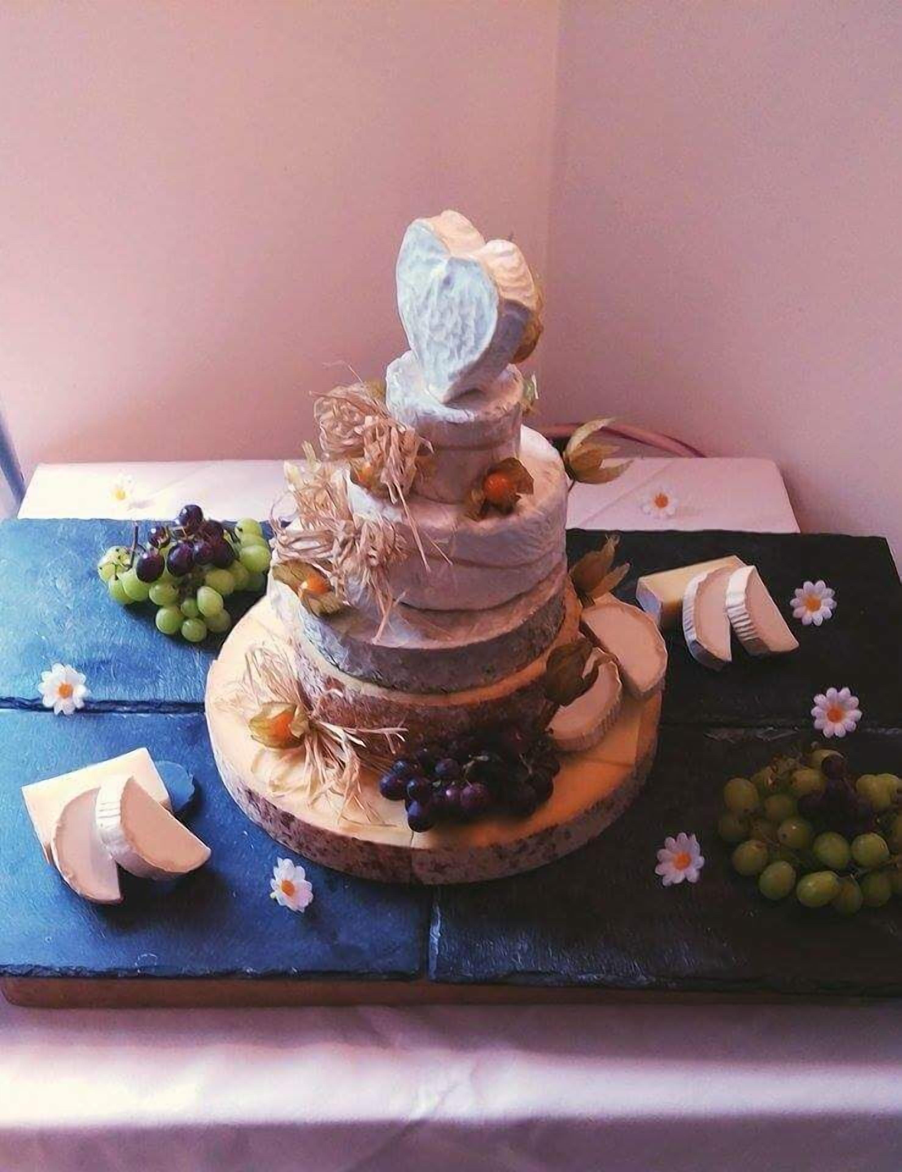 A multi-tiered cake with fruits and flowers on a wooden board.