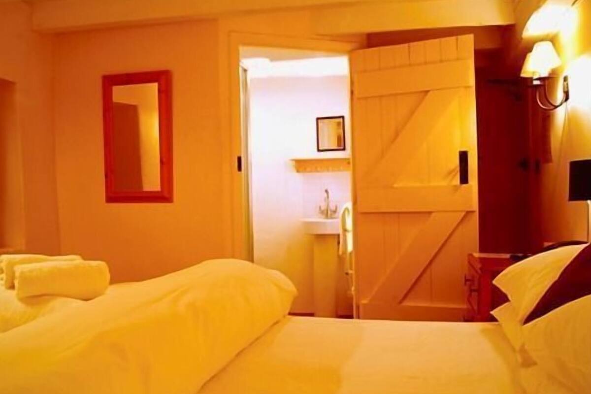 A hotel room with a bed, a door leading to a bathroom, and a wall-mounted light fixture.