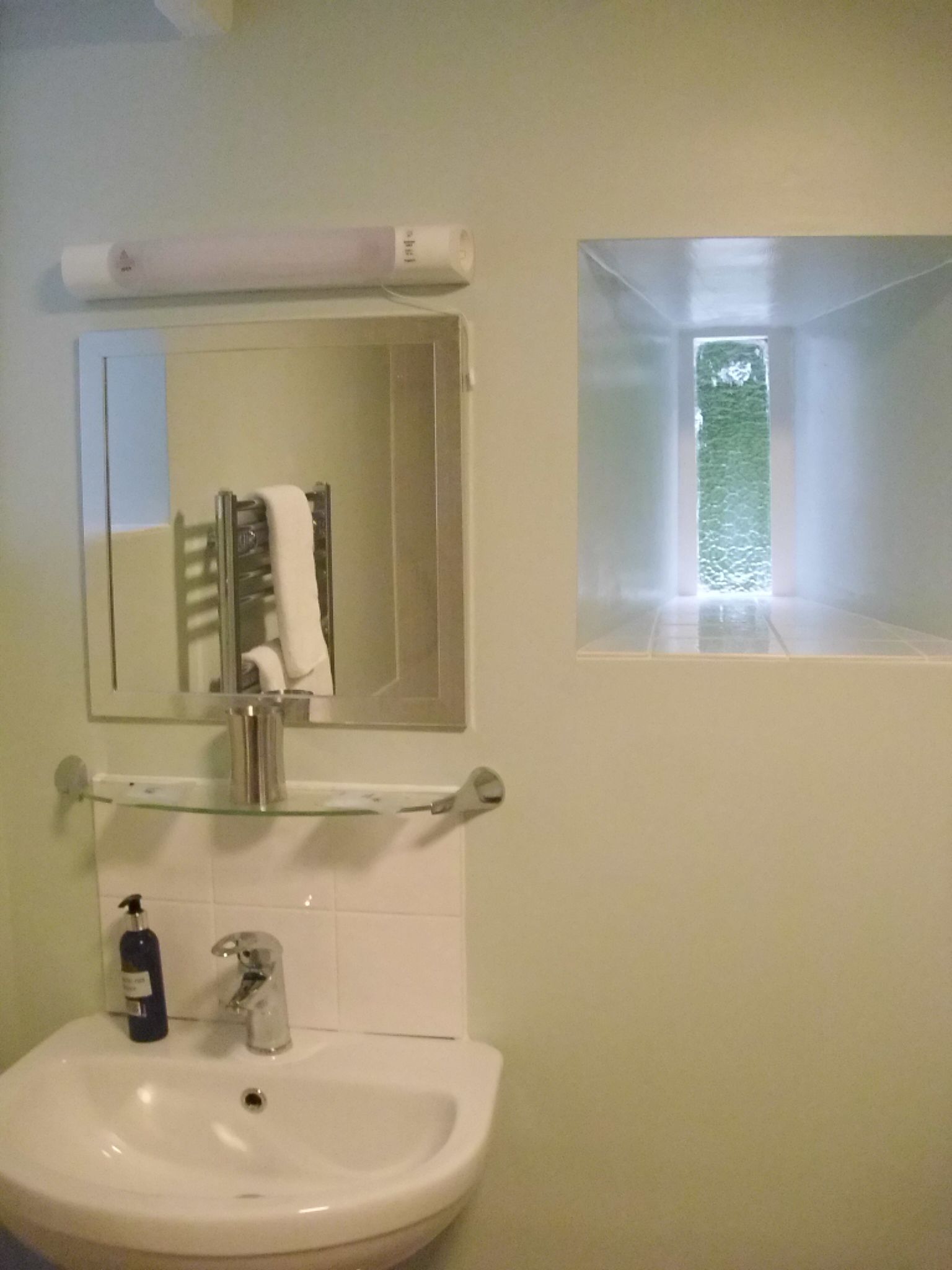 Un baño con un lavamanos blanco, un espejo y un perchero para toallas.