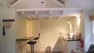 A compact kitchen with a white stone wall, a small bar stool, and a kitchenette area.