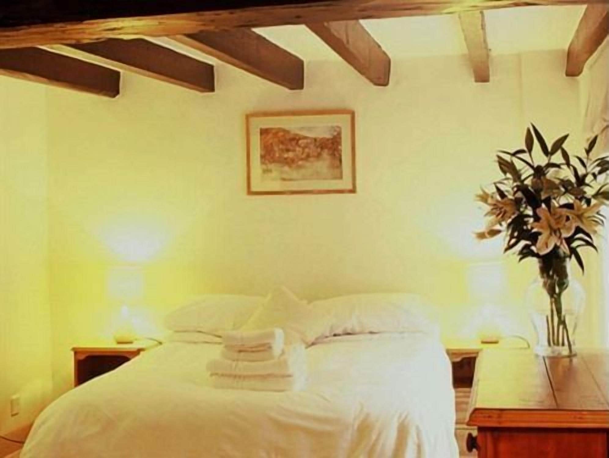 A hotel room with a bed, a nightstand, a vase with flowers, and a painting on the wall.