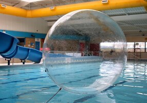 A transparent ball in a swimming pool with a blue slide in the background.