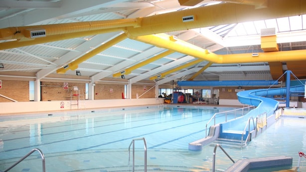 Une piscine intérieure avec des couloirs bien délimités, un toboggan bleu et des poutres de soutien jaunes.
